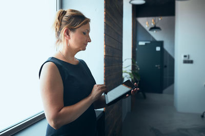 Businesswoman working on tablet in office. mature woman using touch pad computer standing by window