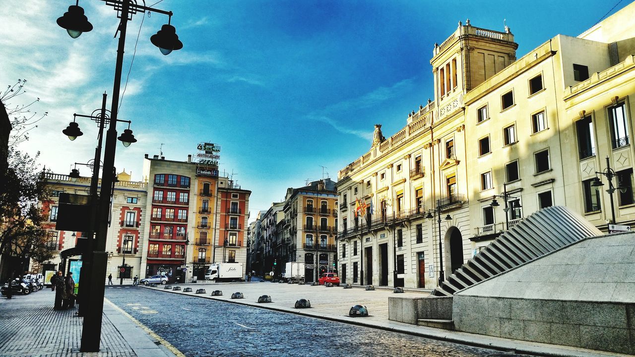 building exterior, architecture, built structure, city, street, sky, street light, residential building, incidental people, building, city life, cobblestone, the way forward, city street, residential structure, day, sunlight, road, outdoors, cloud