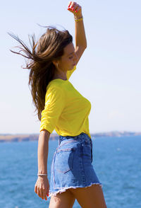 Side view of mid adult woman walking by sea against clear sky during sunny day