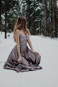 Rear view of woman sitting on snow covered land