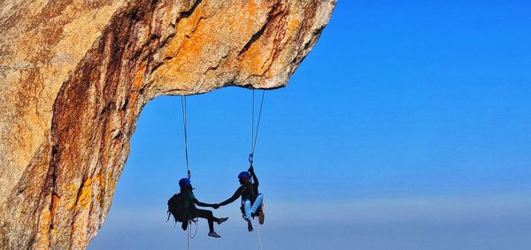 Low angle view of people on rope against sky