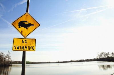 Warning sign by lake against sky