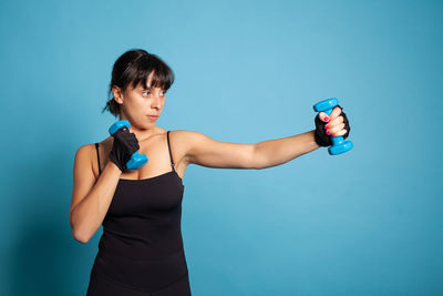 Smiling woman exercising with dumbbells against blue background