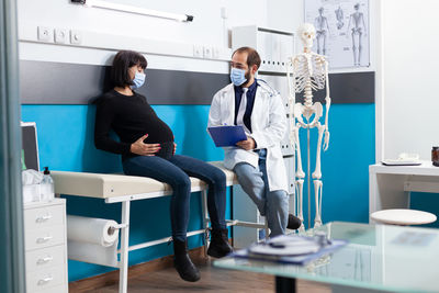 Doctor wearing mask examining pregnant woman in clinic