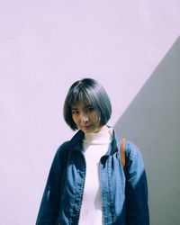 Portrait of smiling young woman standing against white wall