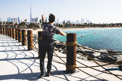 Rear view of man standing by railing against sea