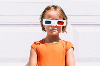 Cute girl in casual colorful clothes and three dimensional glasses standing on white wall background looking at camera