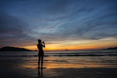 Silhouette woman standing at beach against sky during sunset