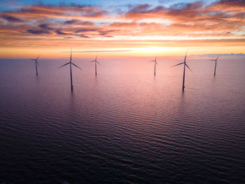 Sunset illuminating wind turbines in ocean, creating stunning natural landscape