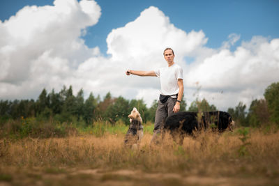 Portrait of young man with dogs on grassy land against sky