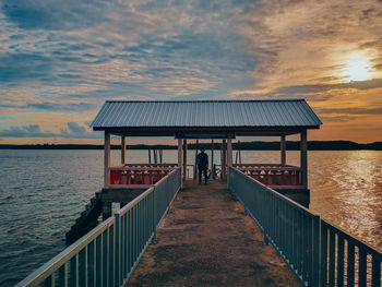 People on pier by sea against sky during sunset