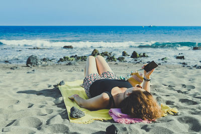 Woman using phone while relaxing at beach