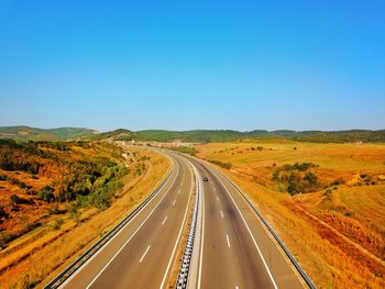 Road passing through landscape against clear blue sky