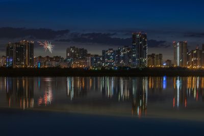 Illuminated buildings by river against sky at night