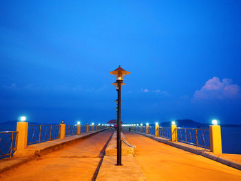 Illuminated street light by sea against blue dusk sky