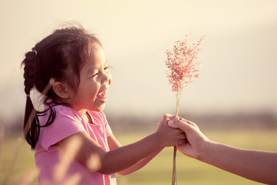 Cropped hand of mother giving flowers to happy daughter against sky