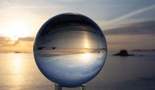 Close-up of crystal ball against sea during sunset