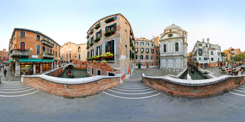 Fish-eye view of canal amidst buildings in city against clear sky