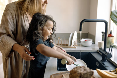 Son helping mother while washing dishes in kitchen sink at home