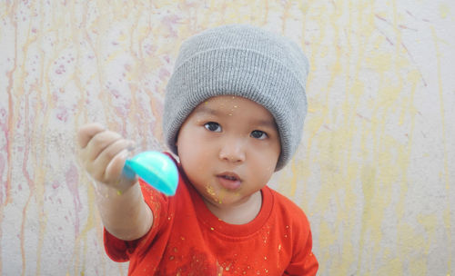 Portrait of cute baby boy holding spoon against wall