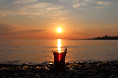 Lit candle on beach against sky during sunset