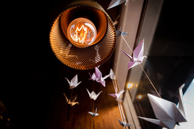 Perspective view from underneath of several origami swans hanging with an old light bulb