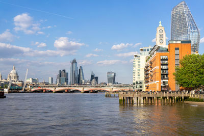 View of city buildings by river against sky