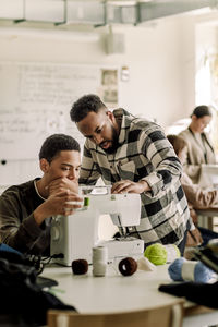 Teacher explaining sewing machine to student in art class at high school