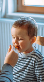 Mom feeds a little boy with a spoon. the boy is sitting on a chair at the table