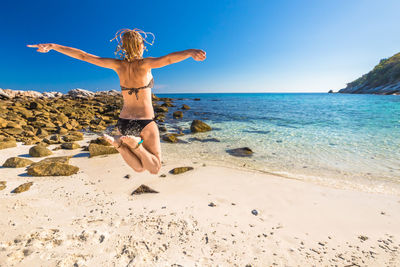 Woman jumping at beach against sky