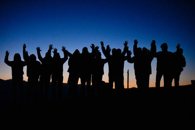 Low angle view of silhouette people standing on field against blue sky at dusk