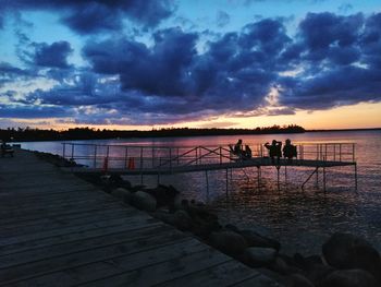 Silhouette people on pier at beach against sky during sunset