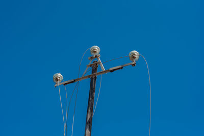 Low angle view of birds on cable against clear blue sky