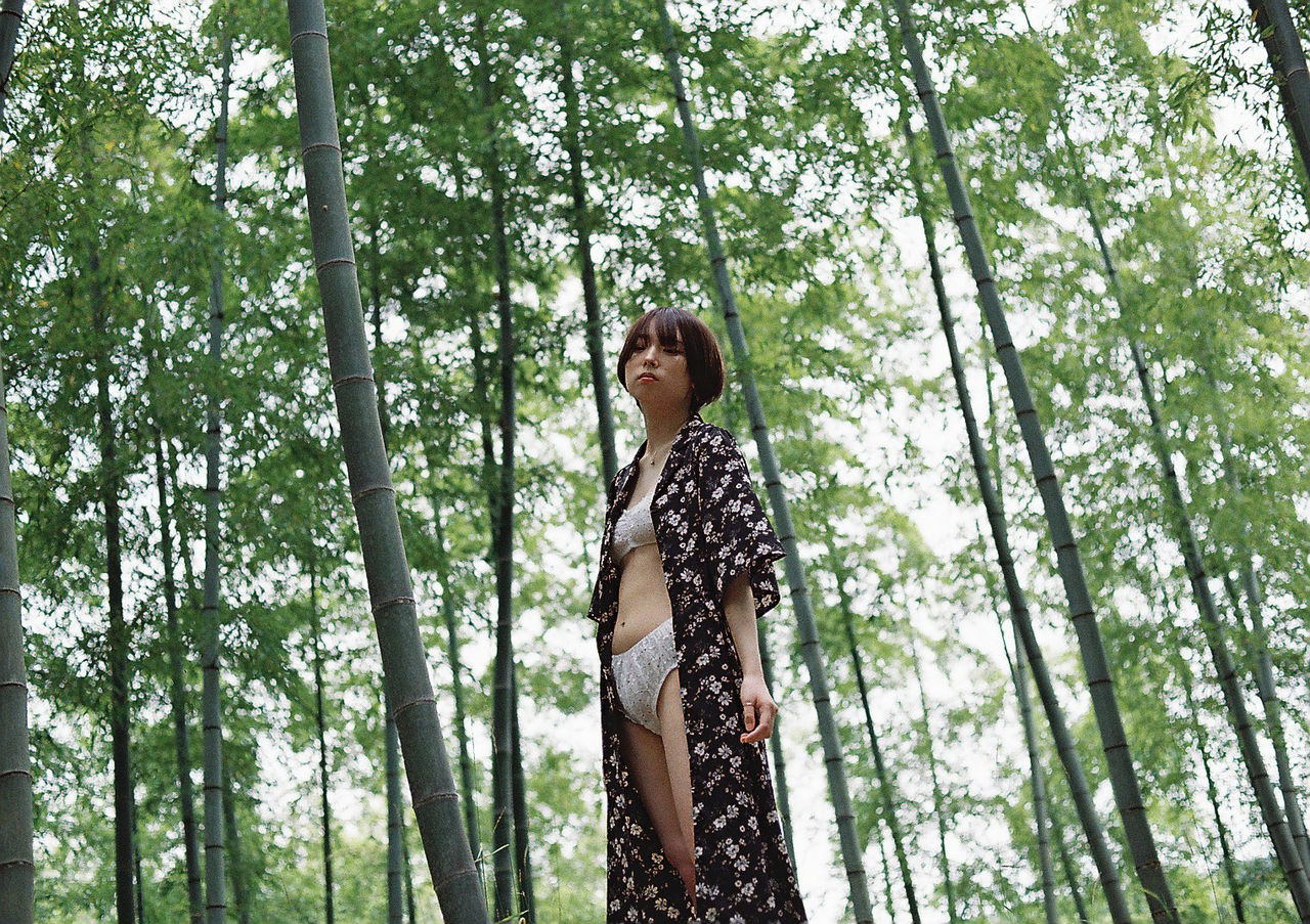 LOW ANGLE VIEW OF YOUNG WOMAN STANDING IN FOREST