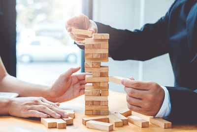 Midsection of businessmen stacking wooden blocks on table