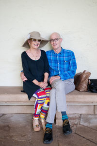 Portrait of senior couple sitting on seat against wall