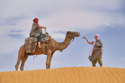 Woman looking at friends sitting on camel in desert