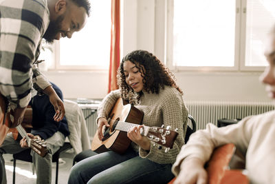 Teenage girl learning to play guitar with male teacher in music class at high school