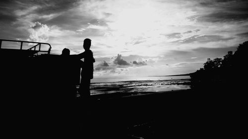 Silhouette people standing by sea against sky during sunset