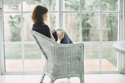 Side view of young woman drinking coffee while sitting by window