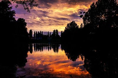 Reflection of trees in calm lake at sunset