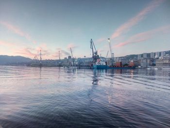 Cranes at harbor against sky during sunset