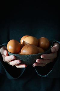 Unusual easter on a dark background. a bowl of brown eggs with hands. darkness, rays of sunlight