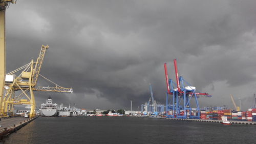 Cranes at commercial dock against cloudy sky