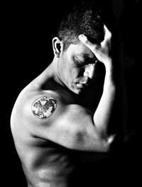 Close-up portrait of shirtless man against black background
