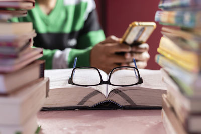 Selective focus on book and glasses through the stack of books while human hands with mobile phone 