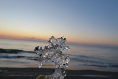 Close-up of snow on beach against sky during sunset