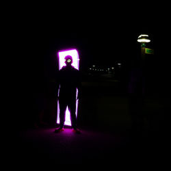 Silhouette man standing against illuminated lights at night