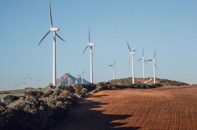 Windmills on landscape against clear blue sky