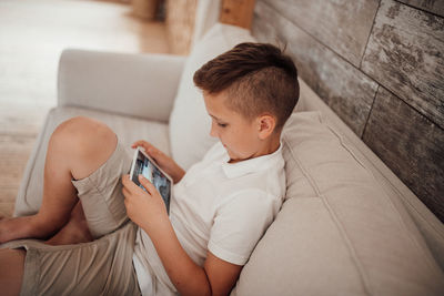 Rear view of boy using mobile phone while sitting on sofa